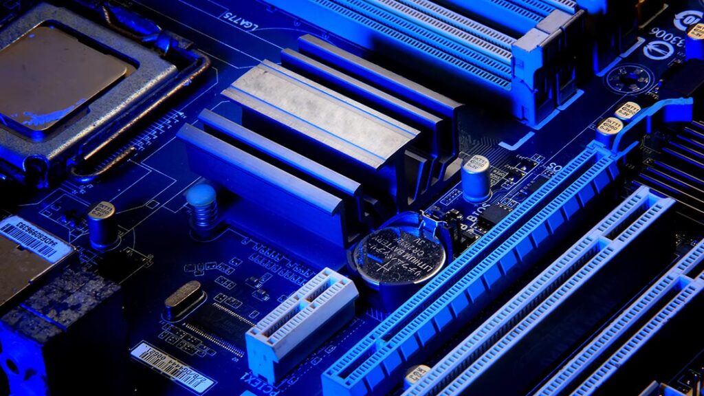 Placa base con componentes como el socket del CPU, ranuras de RAM, condensadores y la batería CMOS visibles.